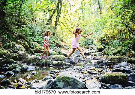 Stock Image - Mixed race sisters exploring stream. Fotosearch