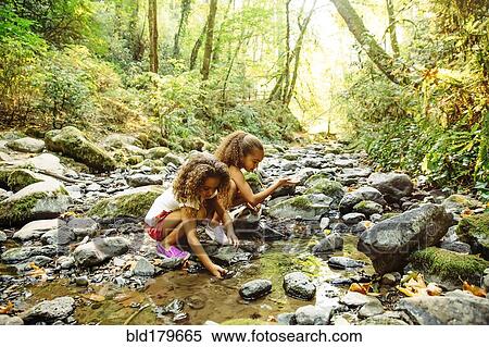 Stock Photography - Mixed race sisters exploring stream. Fotosearch