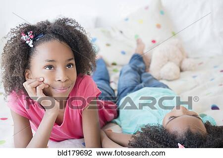 Stock Image - Mixed race sisters laying on bed. Fotosearch