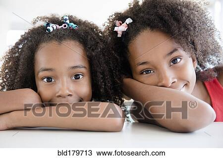 Stock Image - Mixed race sisters leaning on table. Fotosearch