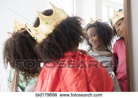 Stock Photo - Mixed race sisters playing dress up in mirror. Fotosearch