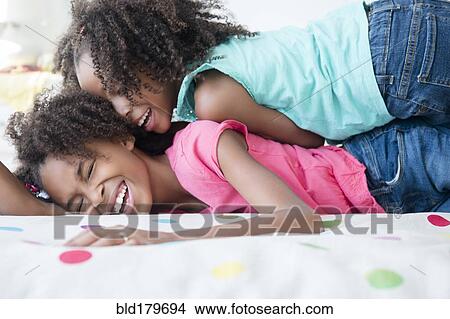 Picture - Mixed race sisters playing on bed. Fotosearch