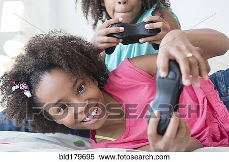Mixed race sisters playing video games on bed View Large Photo Image Stock Photography - Mixed race sisters playing video games on bed. Fotosearch