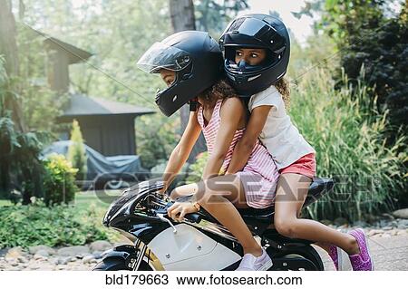 Stock Image - Mixed race sisters riding miniature motorcycle. Fotosearch