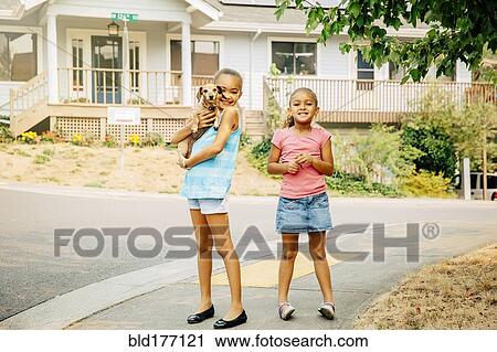 Stock Image - Mixed race sisters smiling on sidewalk. Fotosearch