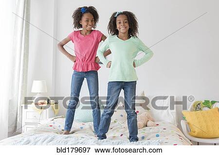 Stock Photo - Mixed race sisters standing on bed. Fotosearch