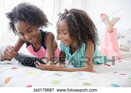 Stock Photo - Mixed race sisters using digital tablet on bed. Fotosearch