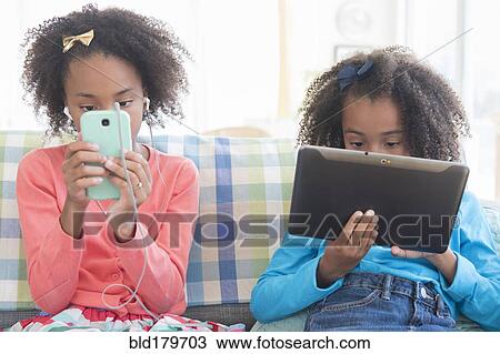 Mixed race sisters using technology on sofa View Large Photo Image Stock Image - Mixed race sisters using technology on sofa. Fotosearch