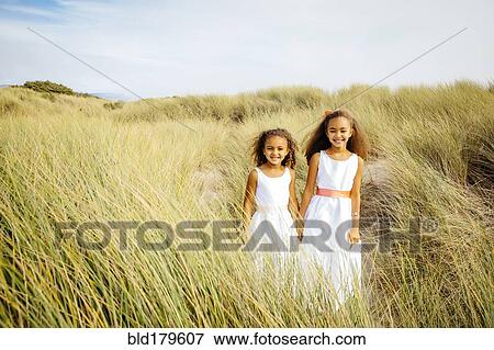Stock Photo - Mixed race sisters walking in grass. Fotosearch