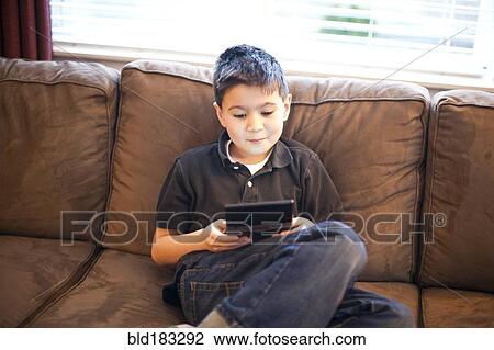 Stock Image - Mixed race teenage boy playing video games on sofa. Fotosearch