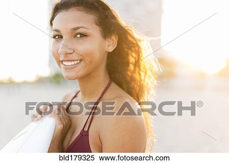 Stock Photography - Mixed race teenage girl carrying surfboard on beach. Fotosearch