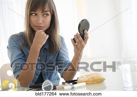 Picture - Mixed race woman admiring herself in mirror. Fotosearch