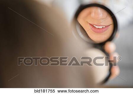 Stock Photography - Mixed race woman admiring herself in compact mirror. Fotosearch