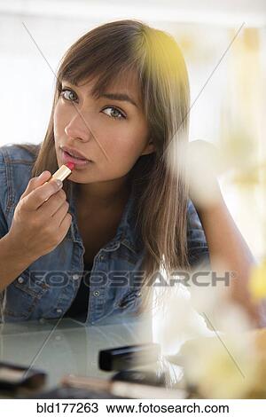 Stock Image - Mixed race woman applying lipstick. Fotosearch