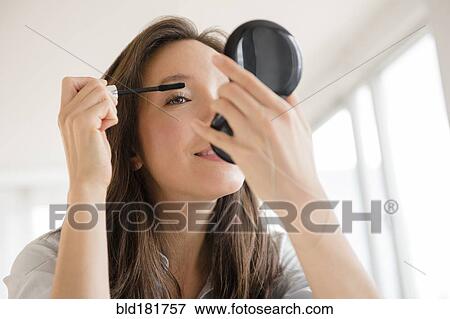 Stock Photo - Mixed race woman applying makeup in compact mirror. Fotosearch