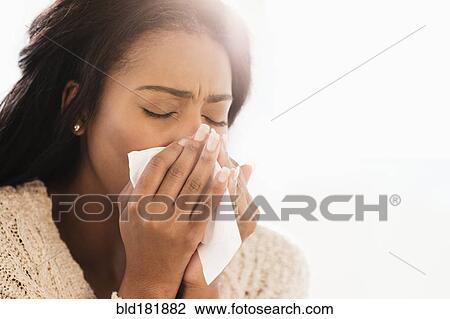 Stock Image - Mixed race woman blowing her nose. Fotosearch