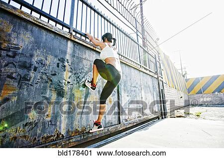 Stock Image - Mixed race woman climbing gate. Fotosearch