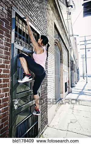 Stock Photo - Mixed race woman climbing gate. Fotosearch