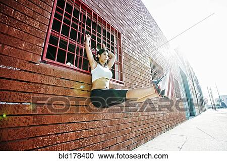 Stock Image - Mixed race woman doing pull-ups on window grate. Fotosearch
