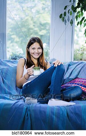 Picture - Mixed race woman drinking coffee on sofa. Fotosearch