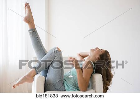 Stock Image - Mixed race woman drinking wine in armchair. Fotosearch