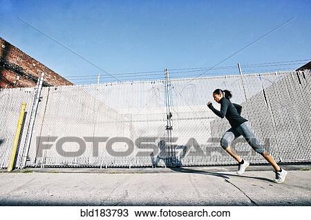 Stock Image - Mixed race woman jogging on sidewalk. Fotosearch