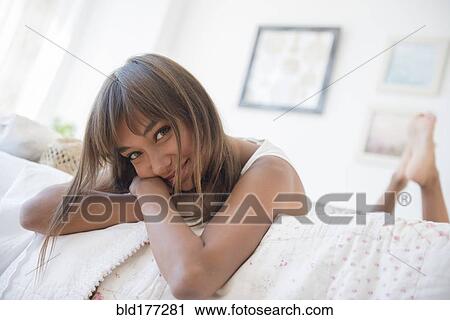 Stock Image - Mixed race woman laying on bed. Fotosearch