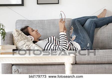Mixed race woman listening to headphones on sofa View Large Photo Image Stock Image - Mixed race woman listening to headphones on sofa. Fotosearch