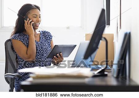 Stock Photograph - Mixed race woman multitasking in office. Fotosearch