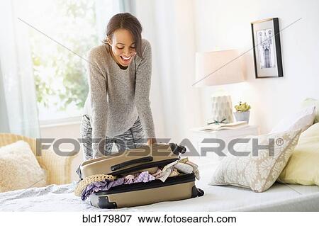 Stock Photo - Mixed race woman packing suitcase in bed. Fotosearch