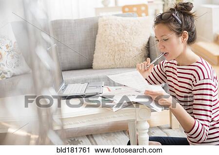 Stock Image - Mixed race woman paying bills on laptop. Fotosearch