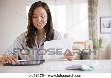 Picture - Mixed race woman paying bills on digital tablet. Fotosearch
