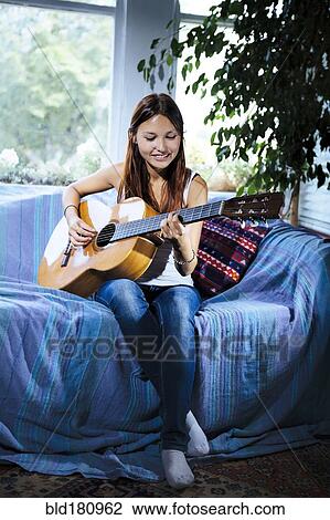 Stock Image - Mixed race woman playing guitar on sofa. Fotosearch