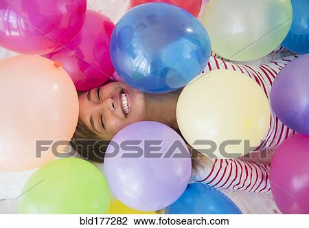 Stock Image - Mixed race woman playing in balloons. Fotosearch