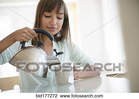 Stock Image - Mixed race woman pouring cup of tea. Fotosearch
