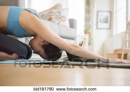 Stock Image - Mixed race woman practicing yoga in living room. Fotosearch