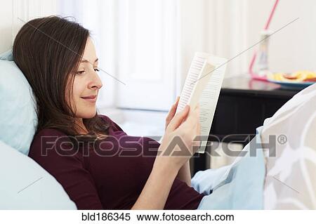 Stock Photography - Mixed race woman reading book in bed. Fotosearch