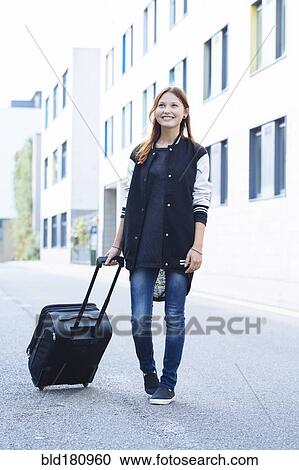 Stock Image - Mixed race woman rolling luggage. Fotosearch