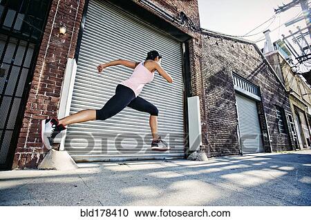 Stock Image - Mixed race woman running on sidewalk. Fotosearch