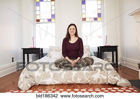 Stock Image - Mixed race woman sitting in bedroom. Fotosearch