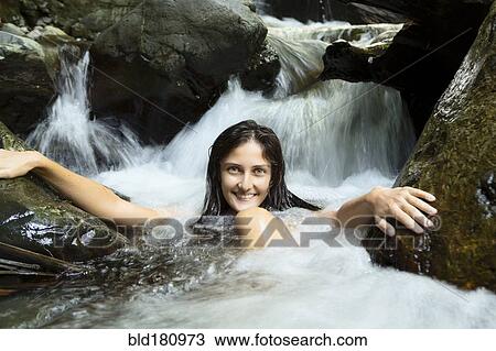 Stock Image - Mixed race woman sitting in waterfall. Fotosearch