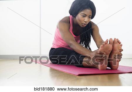 Stock Image - Mixed race woman stretching on yoga mat. Fotosearch