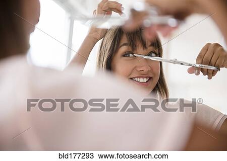 Stock Image - Mixed race woman trimming her bangs. Fotosearch