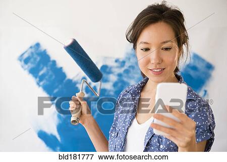Mixed race woman using cell phone and painting wall View Large Photo Image Stock Photo - Mixed race woman using cell phone and painting wall. Fotosearch