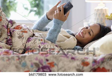 Mixed race woman using cell phone in bed View Large Photo Image Stock Image - Mixed race woman using cell phone in bed. Fotosearch