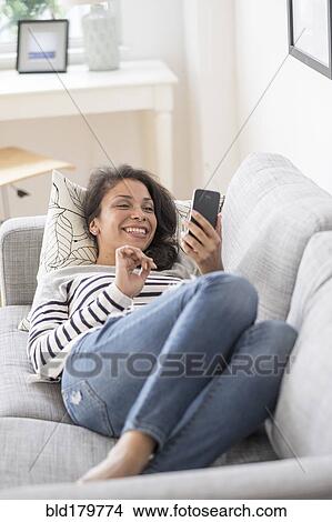 Picture - Mixed race woman using cell phone on sofa. Fotosearch