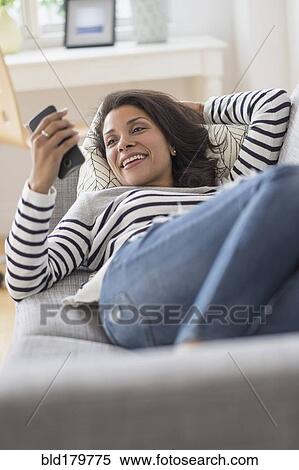 Mixed race woman using cell phone on sofa View Large Photo Image Stock Photography - Mixed race woman using cell phone on sofa. Fotosearch