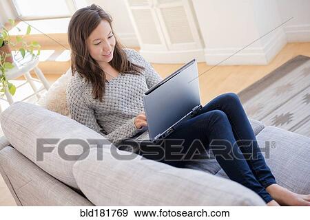 Stock Photo - Mixed race woman using laptop on sofa. Fotosearch