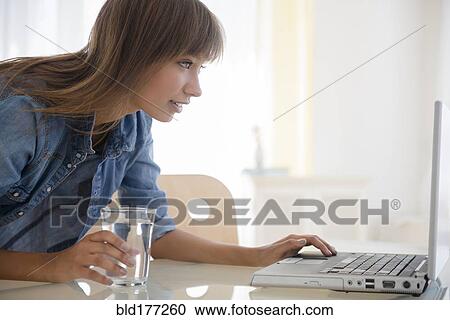 Stock Image - Mixed race woman using laptop on table. Fotosearch