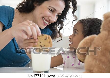 Stock Photograph - Mother and daughter eating milk and cookies. Fotosearch
